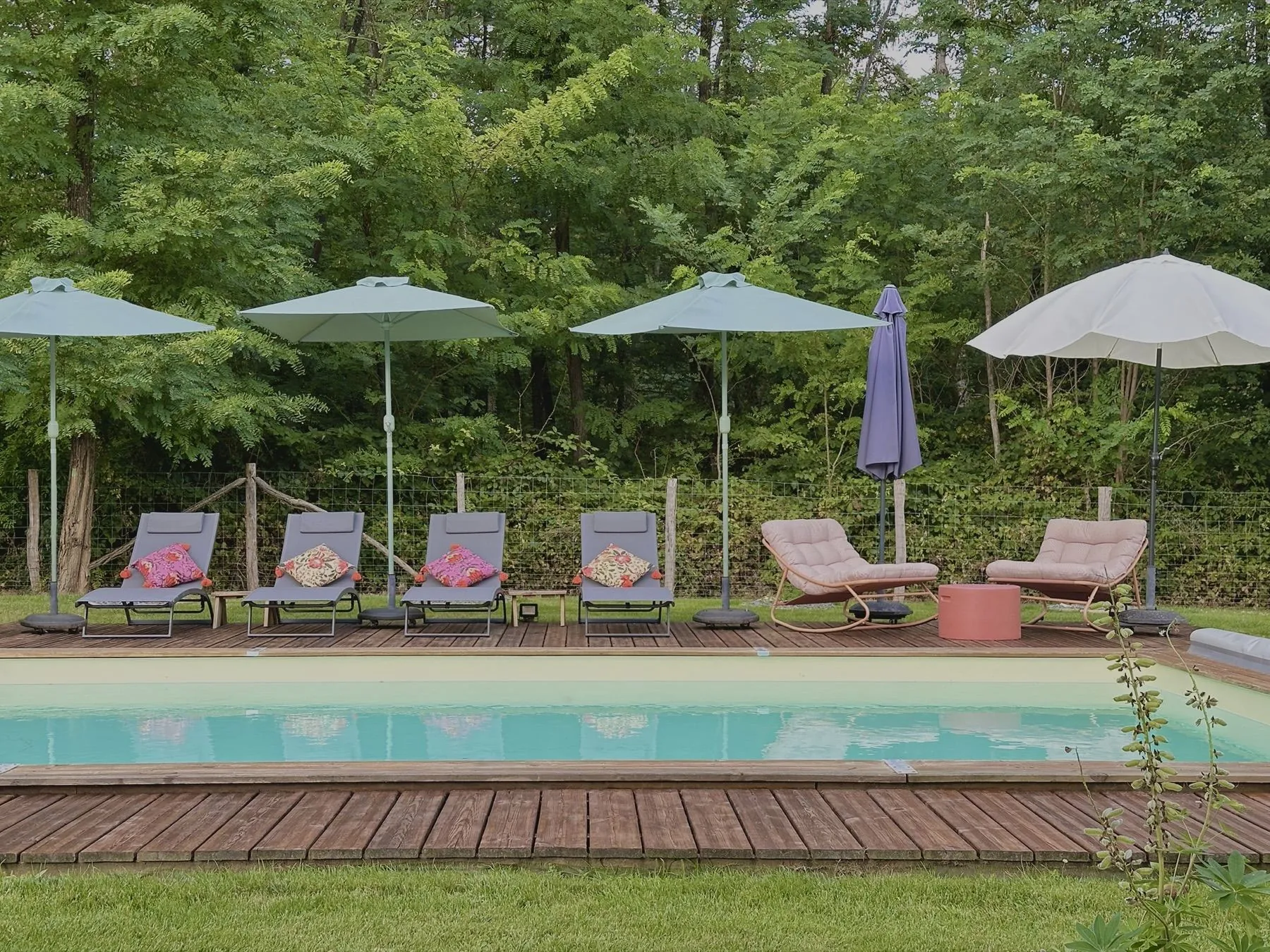 Milasson — piscine bordée de transats et parasols devant les arbres, Atelier Nola